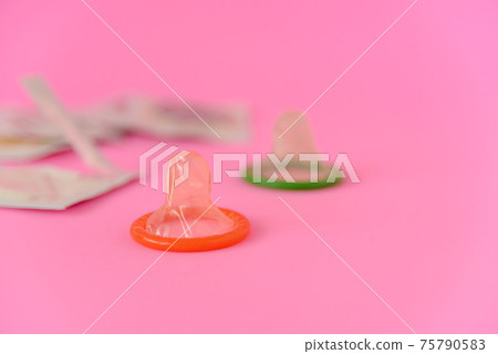Two opened condoms with condom pack on pink paper background with copy space for text. Reproductive health, contraception and safe sex concept 75790583