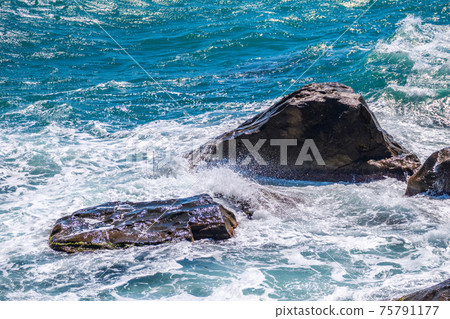 Sea waves of dark water beat against the coastal rocks. An infinite number of splashes, drops of water and white foam are scattered. Sea waves of dark water beat against the coastal rocks. An infinite number of splashes, drops of water and white foam are scattered. 75791177