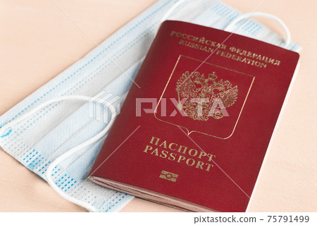 Safe travel during coronavirus pandemic concept. Protective medical mask and Russian passport on the table Safe travel during coronavirus pandemic concept. Protective medical mask and Russian passport on the table 75791499