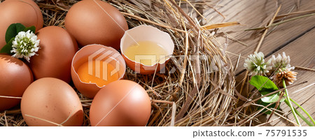 Several raw fresh chicken eggs in a nest of hay on a wooden background, horizontal banner 75791535