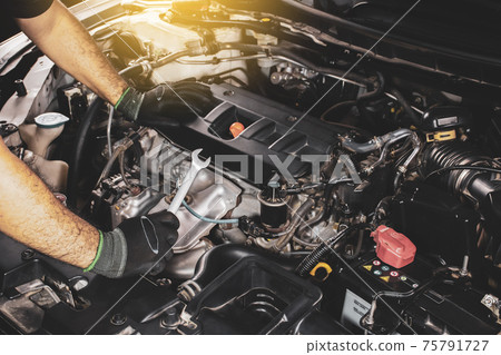 The Mechanic hand holding open-end wrench placed on the car engine with a sunlight 75791727