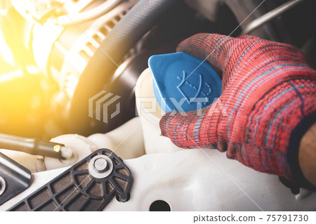 The Mechanic's hand holds is opening lid of the water reserve tank of windscreen wiper 75791730