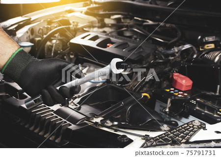 The Mechanic hand holding open-end wrench with a sunlight and engine blurred on background 75791731