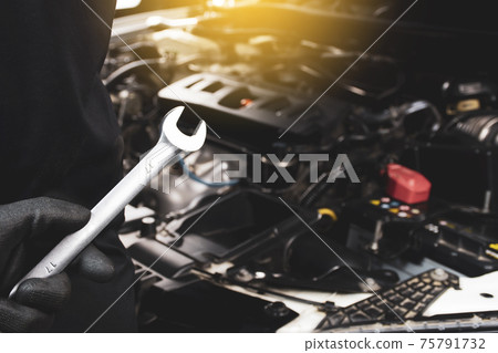 The Mechanic's hand holds wrench behind himself with a sunlight and car engine blurred on background The Mechanic's hand holds wrench behind himself with a sunlight and car engine blurred on background 75791732