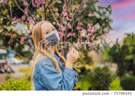 Happy woman in sakura in protective mask and smelling blooming sakura flowers after coronavirus quarantine Happy woman in sakura in protective mask and smelling blooming sakura flowers after coronavirus quarantine 75796445