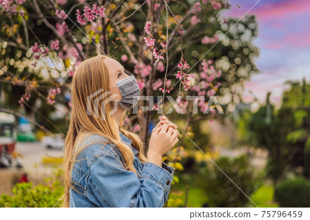 Happy woman in sakura in protective mask and smelling blooming sakura flowers after coronavirus quarantine Happy woman in sakura in protective mask and smelling blooming sakura flowers after coronavirus quarantine 75796459