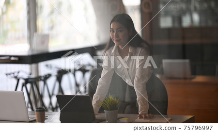 Confident young female office worker standing in office and looking away. Confident young female office worker standing in office and looking away. 75796997