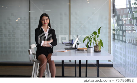 Confident businesswoman sin black suit sitting with arms crossed in modern office. Confident businesswoman sin black suit sitting with arms crossed in modern office. 75796998