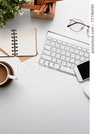 Overhead shot of white office desk with smart phone, notebook, coffee cup, glasses and keyboard. Overhead shot of white office desk with smart phone, notebook, coffee cup, glasses and keyboard. 75796999