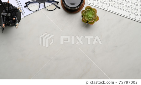 Top view of workplace with keyboard, coffee cup, glasses and  notebook on marble background. Copy space for products display montage. 75797002