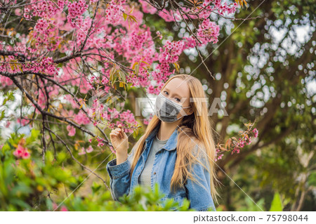 Happy woman in sakura in protective mask and smelling blooming sakura flowers after coronavirus quarantine 75798044