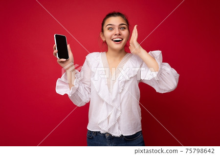 Attractive young happy brunet woman wearing white blouse standing isolated over red background 75798642