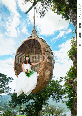 Woman sitting in a bird's nest object in a wedding dress 75799192