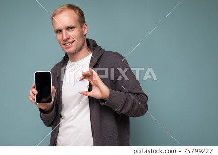 Handsome blonde male person wearing grey sweater and white t-shirt isolated over blue background 75799227