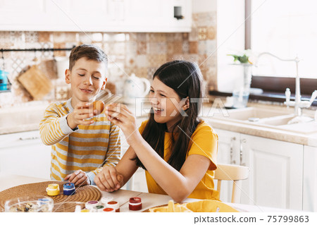 Brother and sister at home in the kitchen paint Easter eggs in different colors for Easter 75799863