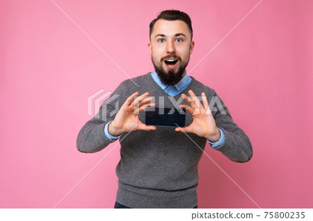 Handsome happy cool young brunette unshaven man with beardwearing stylish grey sweater and blue Handsome happy cool young brunette unshaven man with beardwearing stylish grey sweater and blue 75800235