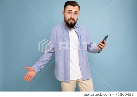 Upset handsome young brunette unshaven man with beard wearing stylish white t-shirt and blue shirt 75800428