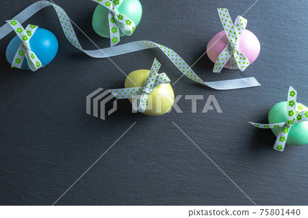 Easter background blue. Colourful egg with tape ribbon on dark rough stone background in Happy Easter decoration. Flat lay, top view. Easter background blue. Colourful egg with tape ribbon on dark rough stone background in Happy Easter decoration. Flat lay, top view. 75801440