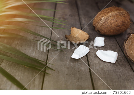 Broken coconuts on gray wooden background with palm leaf. White coconut pulp Broken coconuts on gray wooden background with palm leaf. White coconut pulp 75801663