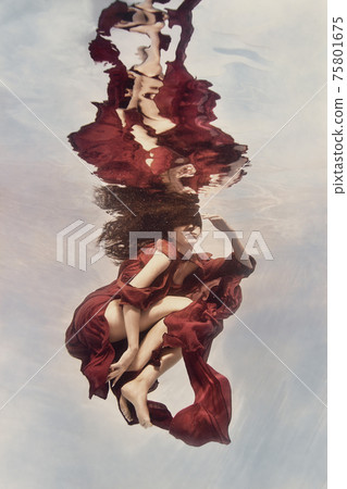 A girl in a fluttering red dress swims underwater as if flying in zero gravity 75801675