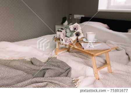 Coffee table on bed. Flowers, cup, note pad, pen. Interior gray interior, plaid 75801677