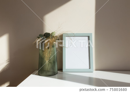 Glass vase with herbarium flowers, eucalyptus branches, empty white photo frames 75801680