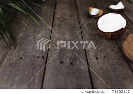 Broken coconuts on gray wooden background with palm leaf. White coconut pulp Broken coconuts on gray wooden background with palm leaf. White coconut pulp 75802167