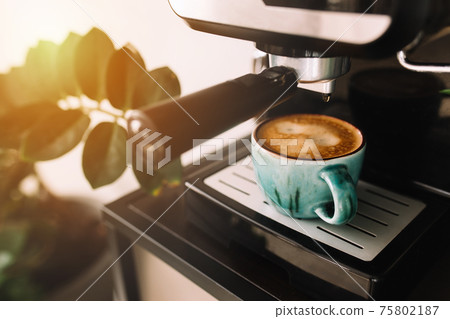 Green cup of coffee at the coffee maker machine, coffee time. Blurred background 75802187