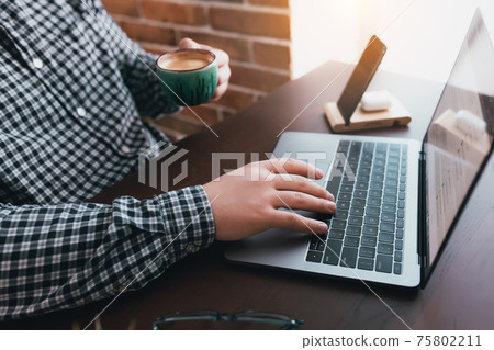 Man working at the laptop with a cup of coffee at home. Blurred background Man working at the laptop with a cup of coffee at home. Blurred background 75802211