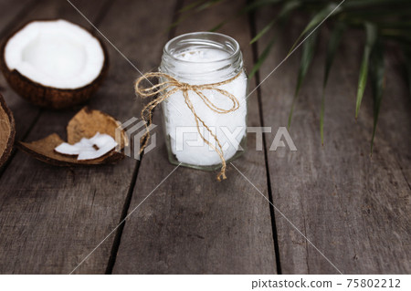 Broken coconuts on gray wooden background with oil jar. White coconut pulp Broken coconuts on gray wooden background with oil jar. White coconut pulp 75802212