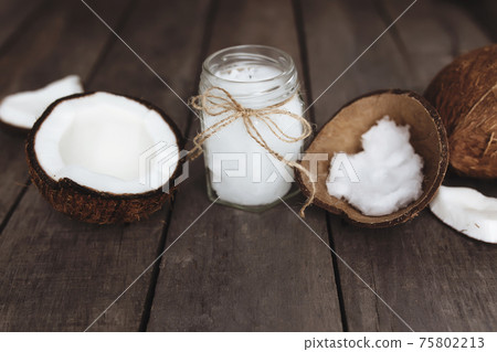 Broken coconuts on gray wooden background with oil jar. White coconut pulp Broken coconuts on gray wooden background with oil jar. White coconut pulp 75802213