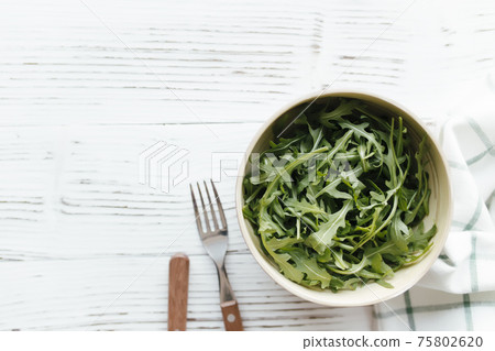 Green arugula salad leaves in bowl on wooden background. Healthy eating concept Green arugula salad leaves in bowl on wooden background. Healthy eating concept 75802620