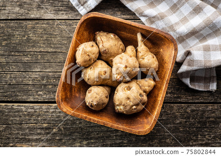 Raw jerusalem artichoke. Topinambur vegetable root in wooden bowl. Raw jerusalem artichoke. Topinambur vegetable root in wooden bowl. 75802844