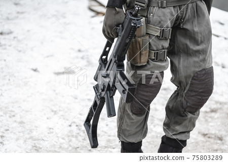 A military man with a machine gun down is walking along the road. A military man with a machine gun down is walking along the road. 75803289