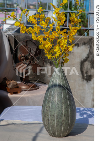 Bouquet of yellow flowers in Green watermel on shape ceramic vase and old vintage fan on pink textured table cloth with old cement wall at the balcony house. 75803578