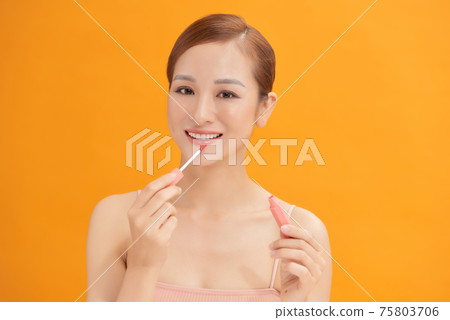 Beauty portrait of a pretty young topless woman wearing makeup isolated over yellow background, applying lip gloss 75803706