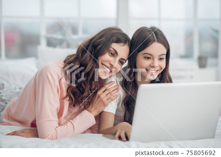 Daughter and mom looking at laptop in good mood Daughter and mom looking at laptop in good mood 75805692