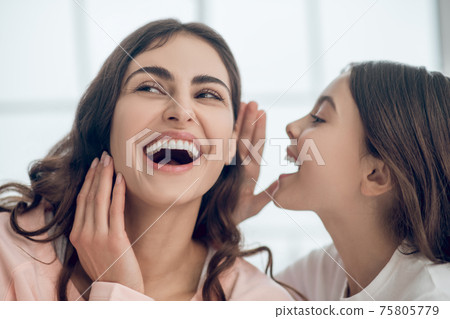 Daughter speaking in ear of laughing mother Daughter speaking in ear of laughing mother 75805779