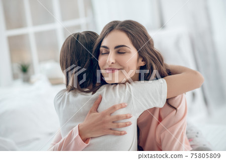 Happy mom with closed eyes hugging daughter tightly Happy mom with closed eyes hugging daughter tightly 75805809