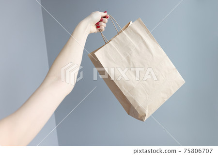 Womans hand holding paper shopping bag closeup 75806707