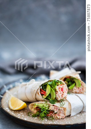 Fresh and healthy wrapped tortilla with crab salad, cucumber, avocado, pepper and green herbs 75807873