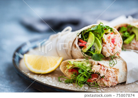 Fresh and healthy wrapped tortilla with crab salad, cucumber, avocado, pepper and green herbs 75807874