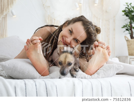 Young positive woman lying on the bed and having fun with her dog xoloitzcuintli 75812836
