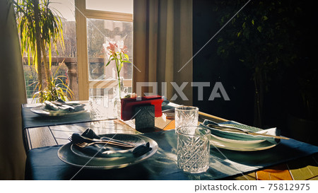 Table setting for romantic breakfast in the morning sun through a window. Shadows and sunbeams in dark room. Table setting for romantic breakfast in the morning sun through a window. Shadows and sunbeams in dark room. 75812975