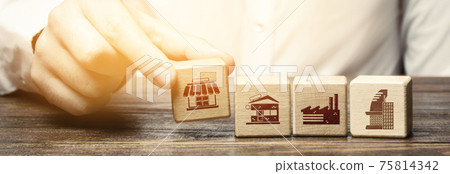 A man lays in a row blocks with symbols of business shops, offices and factories. Building a successful business empire. Investments. Merge small competitors, expansion. Franchise concept. 75814342