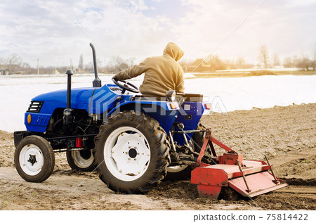 Farmer on a tractor with milling machine loosens, grinds and mixes soil. Loosening the surface, cultivating the land for further planting. Farming and agriculture. Cultivates the soil. Plows a field. 75814422