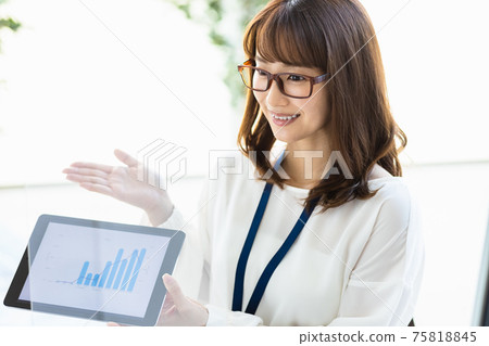 A woman talking over an acrylic partition while showing materials on a tablet PC A woman talking over an acrylic partition while showing materials on a tablet PC 75818845