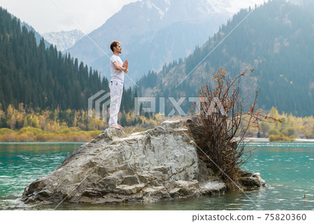 A man in a Samasthiti pose on a stone among a mountain lake. A man in a Samasthiti pose on a stone among a mountain lake. 75820360