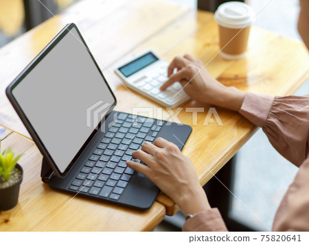 Female office worker using digital tablet and calculator on wooden table in cafe Female office worker using digital tablet and calculator on wooden table in cafe 75820641