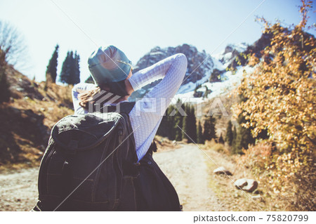 A brunette with a backpack stretches in the sun. Clear sky in the mountains. A brunette with a backpack stretches in the sun. Clear sky in the mountains. 75820799